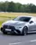 A silver Mercedes-AMG speeding on a test track at Mercedes-Benz World, with the driver focused and blurred trees and grass in the background.