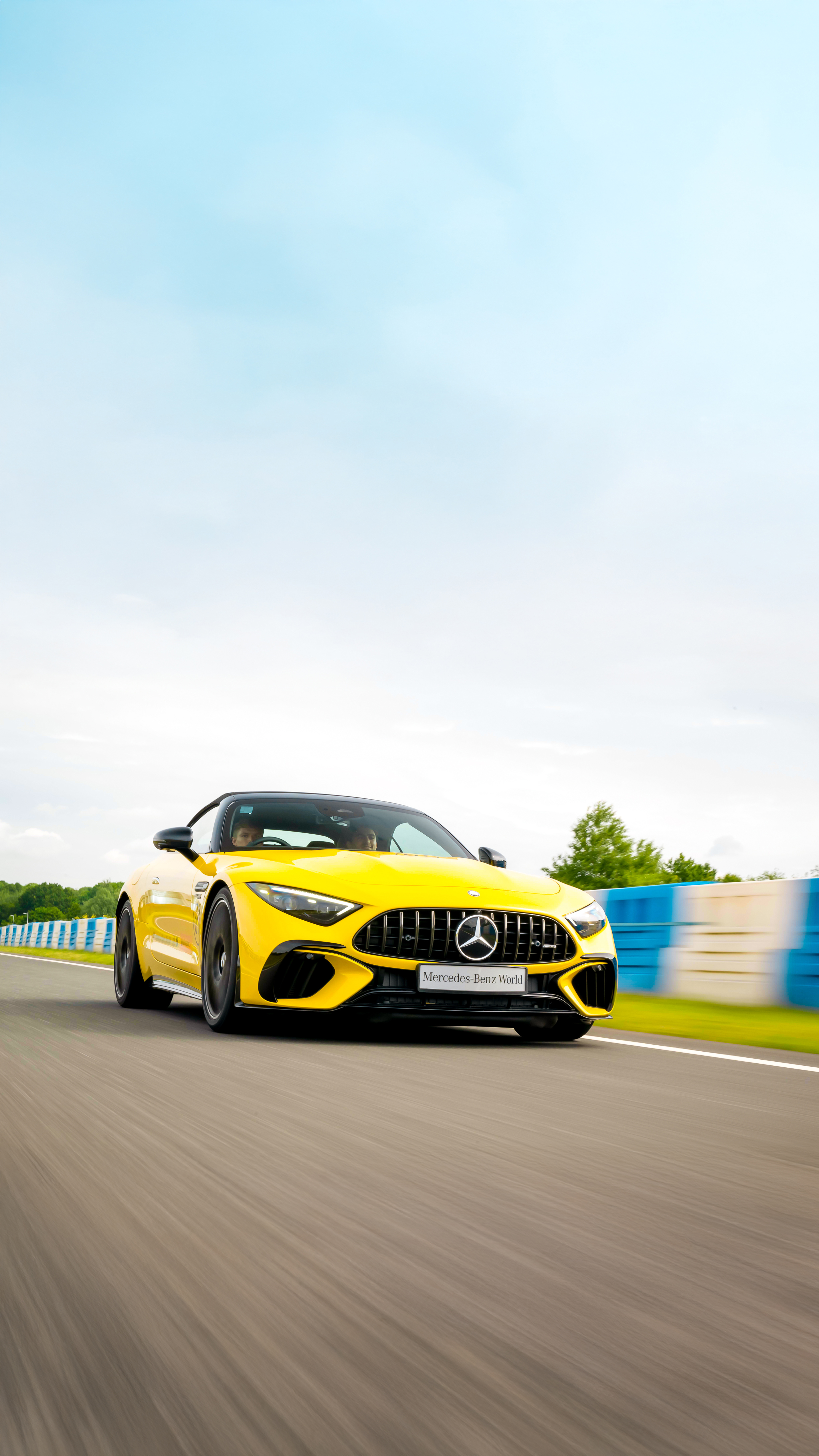 Bright yellow Mercedes-AMG sports car speeding down the track at Mercedes-Benz World, showcasing sleek design and high-performance engineering.