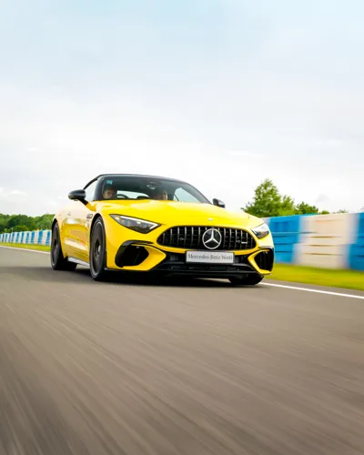 Bright yellow Mercedes-AMG sports car speeding down the track at Mercedes-Benz World, showcasing sleek design and high-performance engineering.