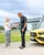Young girl shaking hands with a Mercedes-Benz instructor outside Mercedes-Benz World, next to a bright yellow vehicle, symbolizing a positive learning experience.