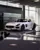 White Mercedes-AMG SLS Black Series on display inside Mercedes-Benz World, spotlighted in a showroom setting with reflective floors and digital backdrop.