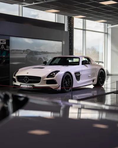 White Mercedes-AMG SLS Black Series on display inside Mercedes-Benz World, spotlighted in a showroom setting with reflective floors and digital backdrop.