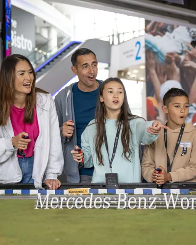 Family enjoying a hands-on racing activity with remote-controlled cars at Mercedes-Benz World, engaging with excitement around a mini track exhibit.