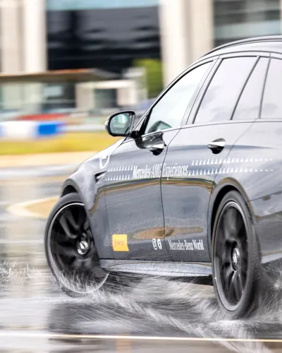 Close-up of a Mercedes-AMG vehicle drifting on a wet handling track at Mercedes-Benz World, showcasing precision control and performance in challenging conditions.