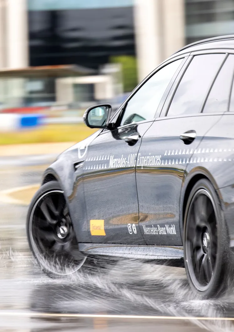 Close-up of a Mercedes-AMG vehicle drifting on a wet handling track at Mercedes-Benz World, showcasing precision control and performance in challenging conditions.