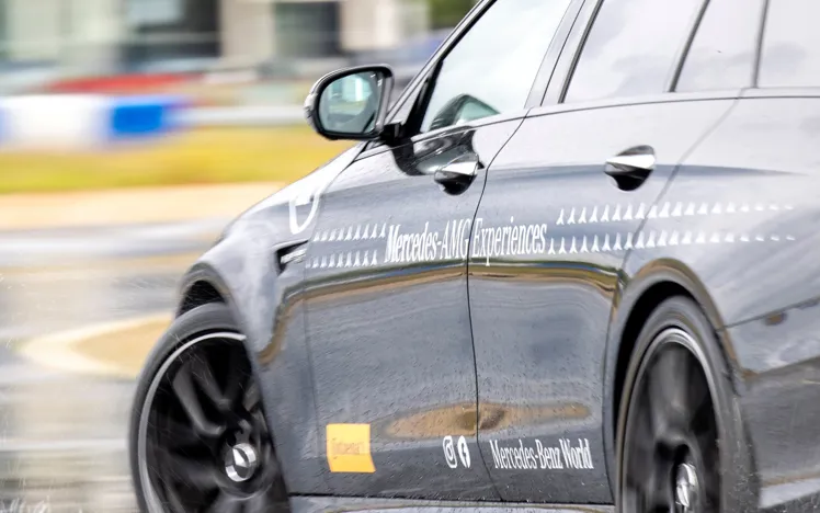 Close-up of a Mercedes-AMG vehicle drifting on a wet handling track at Mercedes-Benz World, showcasing precision control and performance in challenging conditions.
