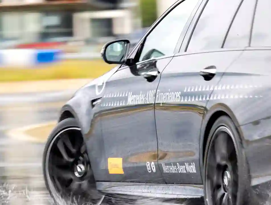 Close-up of a Mercedes-AMG vehicle drifting on a wet handling track at Mercedes-Benz World, showcasing precision control and performance in challenging conditions.